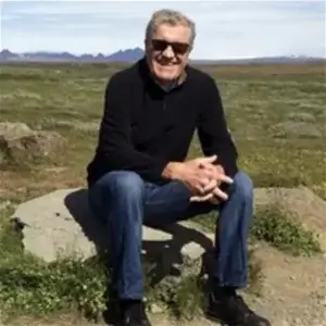 Hannu sitting outside on a rock in a grassy area.