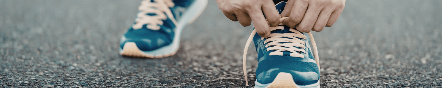 A man lacing up his blue running shoes on pavement.