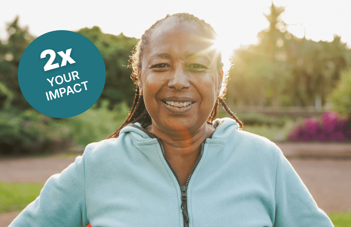 A woman standing in a field in the sun wearing an athletic sweater. Text reads: "2x your impact"