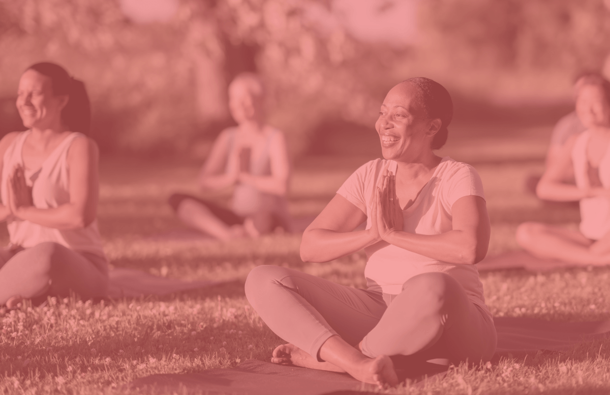 A group of women seated on yoga mats on the grass.