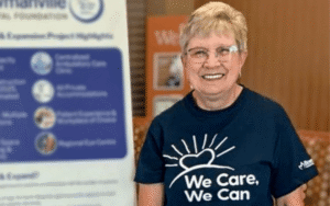 Isabel wearing a We Care, We Can t-shirt and standing in front of a Bowmanville Hospital Foundation sign.