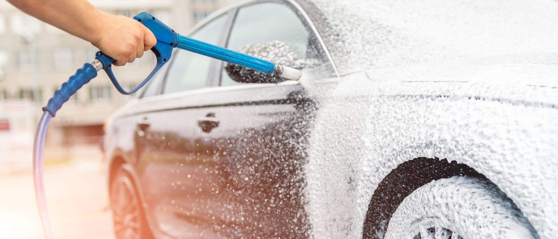 A person hosing down a black car.