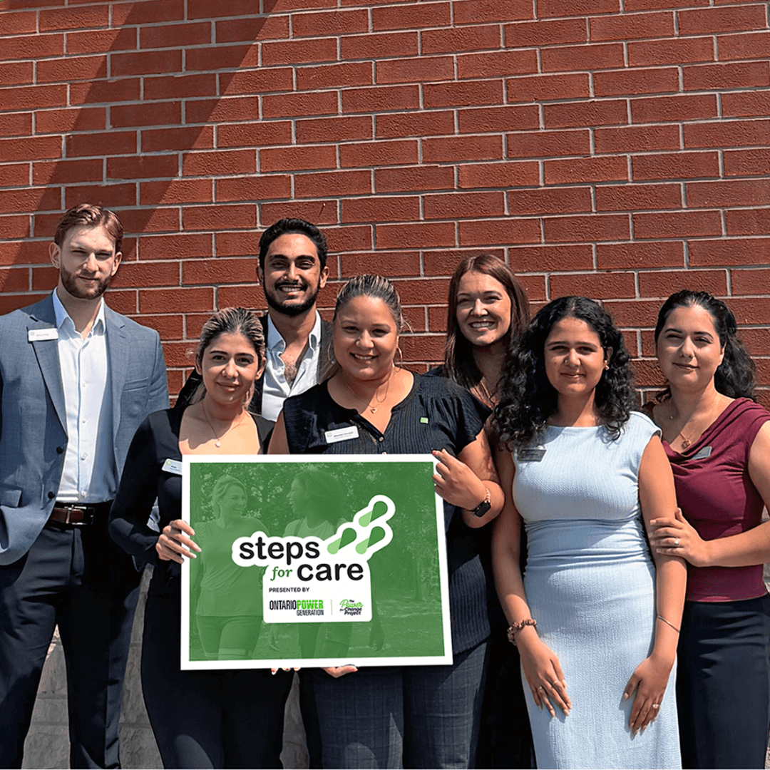 A group of TD employees in front of a brick wall, holding a Steps for Care sign.